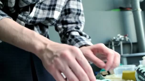 Młody mężczyzna sznuruje stylowe trampki przy stole w warsztacie naprawczym — Wideo stockowe
