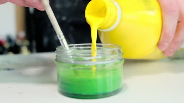 Człowiek wlewa żółtą farbę do szklanego słoika mieszając zielony kolor — Wideo stockowe