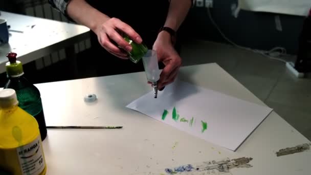 男人在饭桌上把绿色油漆倒入装有喷雾器的容器 — 图库视频影像