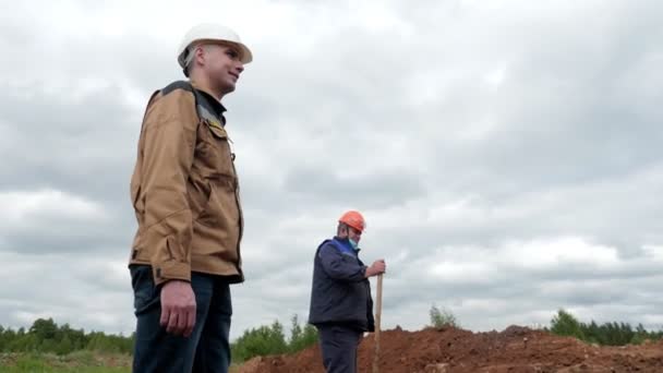 Arbeiter in Uniform stehen neben Bagger, der Graben ausheben will — Stockvideo