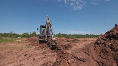 Kazıcı inşaat alanındaki hendeğin yakınına kahverengi toprak döker.