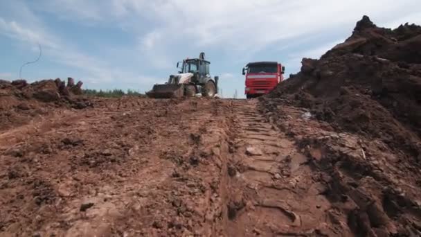 Movimento ao longo da estrada suja para escavadeira e caminhão basculante vermelho — Vídeo de Stock