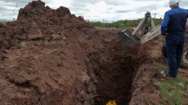 İşçiler yakınlarda dururken buldozer sipere toprak döker.