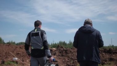 İşçi, meslektaşıyla birlikte petrol sahasında yürüyen kablo bobini taşıyor.