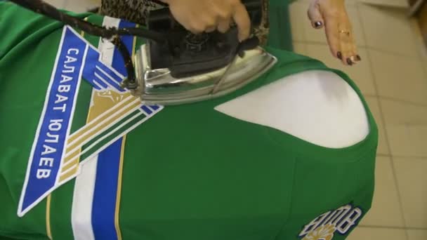 Работник гладит зеленую хоккейную форму рубашки на верстаке — стоковое видео