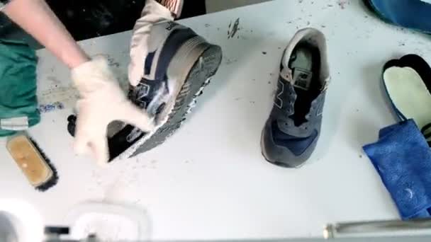 Mitarbeiterin wäscht Ledersneaker an weißem Tisch im Geschäft