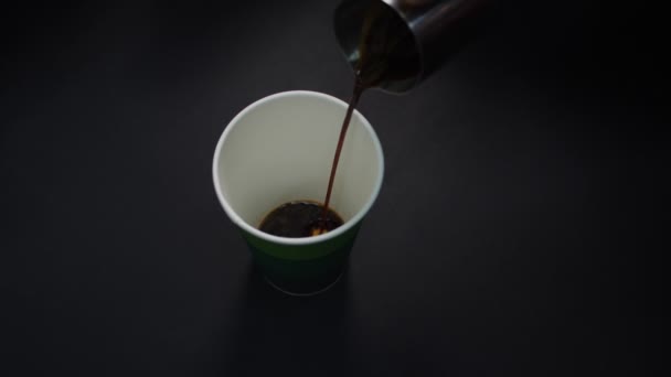 Menuangkan kopi segar ke dalam cangkir kertas dari kendi di atas meja hitam — Stok Video