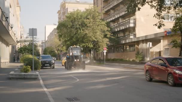 Ciągnik oczyszcza drogę z wody jazdy wzdłuż ulicy miasta — Wideo stockowe
