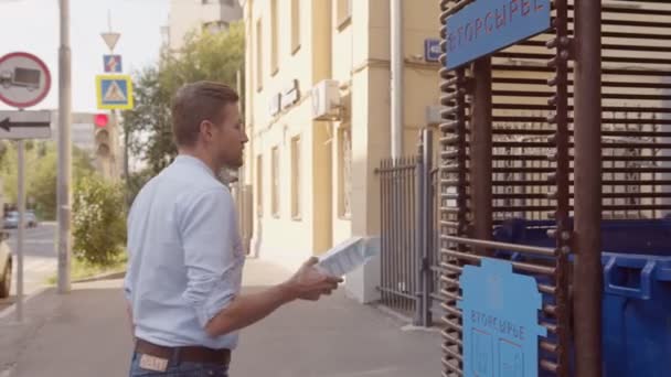 Junger Mann wirft Getränkeverpackungen in Mülleimer auf Straße — Stockvideo