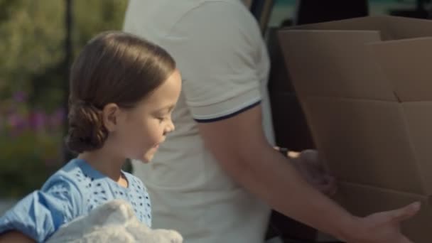 女の子は車のトランクに持ち物を入れて母親におもちゃを与えます — ストック動画