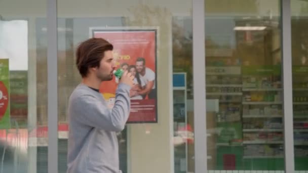 Kerl im grauen Pullover trinkt Getränke und läuft an Geschäften vorbei — Stockvideo