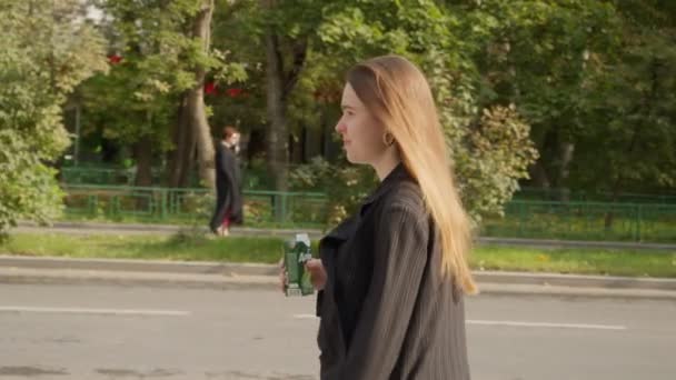 Mulher bebe bebida do pacote andando ao longo da rua — Vídeo de Stock