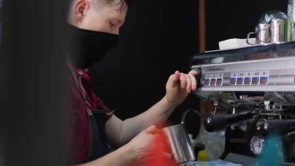 El hombre en la máscara bate la leche con la máquina y vierte la bebida en la taza — Vídeos de Stock