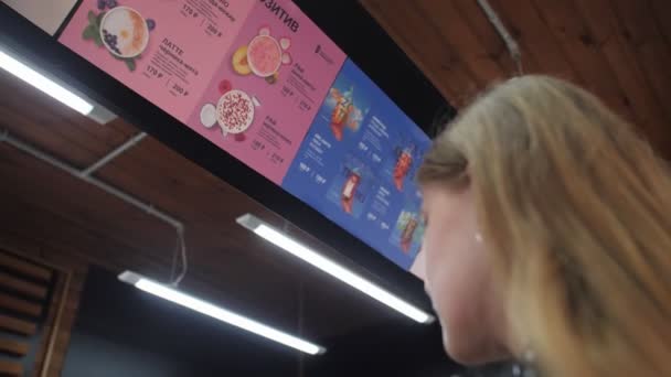 Jonge vrouw kiest koffie kijken naar menu onder het plafond — Stockvideo