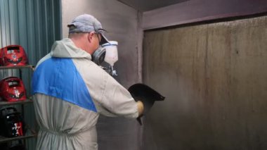 Çalışan, egzoz vantilatörünün yanındaki kaynakçı maskesine lakquer uygular