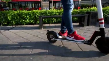 Spor ayakkabısı giyen biri, set boyunca e-scooter kullanır.