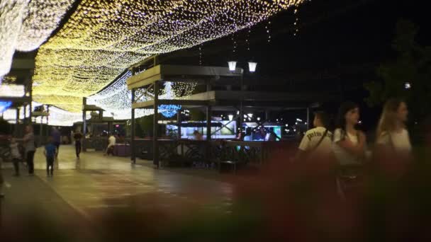 Férfiak és nők sétálnak a töltésen ragyogó fényekkel — Stock videók