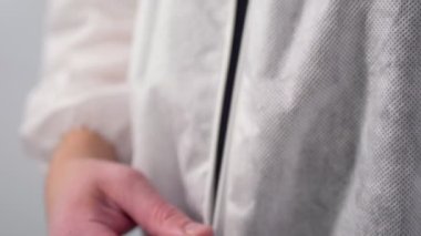 Adam gri üzerine beyaz, tek kullanımlık koruyucu üniforma giyiyor.