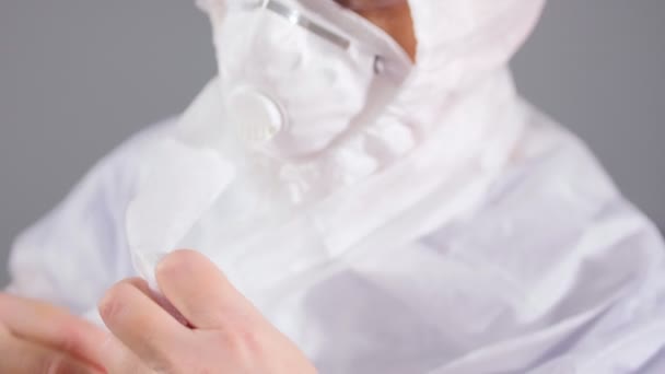 Medical worker in respirator ties hood bands on light grey — Stock Video