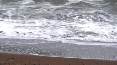 Kışın kumsalda köpüklü deniz dalgaları yuvarlanıyor.