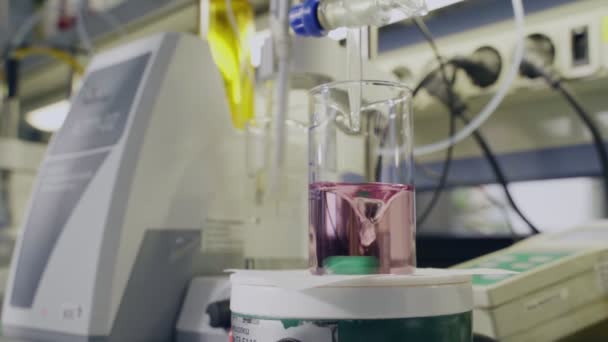 Utrustning blandar rosa vätska i glasbägare i anläggningslabb — Stockvideo