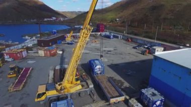 Sarı vinç yüklü kamyon okyanus kıyısındaki büyük bir deponun yakınında.