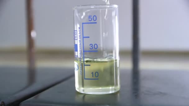 Капание прозрачного нефтепродукта в небольшой стакан на столе — стоковое видео