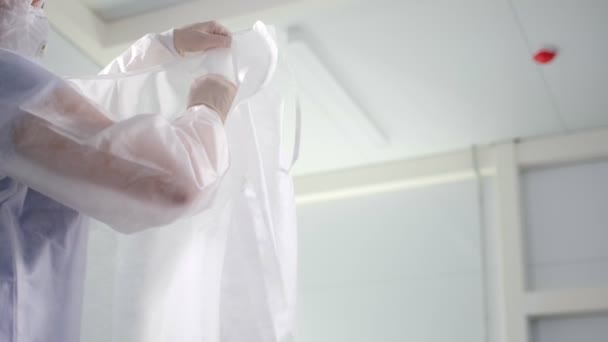 Läkaren sätter på sig engångs skyddsrock i ljusrummet — Stockvideo