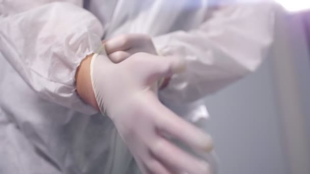 Ο γιατρός με προστατευτικά ρούχα φοράει γάντια στο γκρι. — Αρχείο Βίντεο