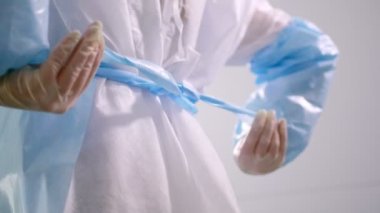 Tek kullanımlık koruyucu elbise giyen işçi önlük bantları bağlar