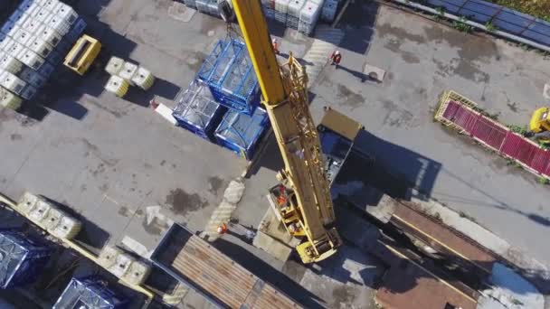 Грузовой кран поднимает контейнер под контролем рабочих во дворе — стоковое видео