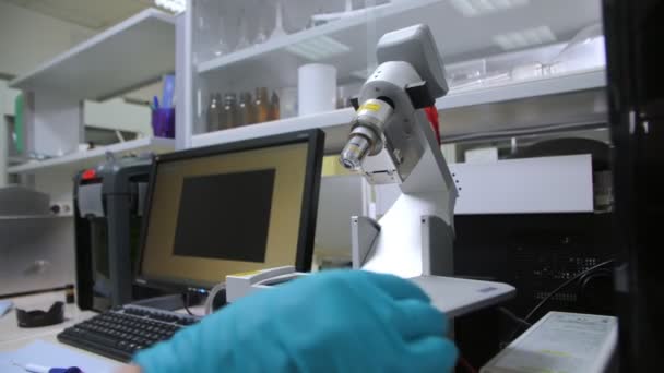 Empregado coloca parte com amostra sob microscópio em laboratório — Vídeo de Stock