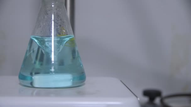 Mezcla de líquido azul claro en Erlenmeyer frasco en primer plano de laboratorio — Vídeo de stock