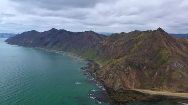 曇り空の下、穏やかな海の海岸にある古い山 — ストック動画