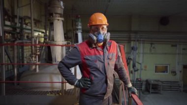 Üniformalı ve miğferli bir işçi, tankın yanında solunum cihazı var.