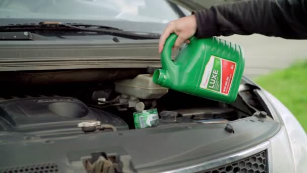 Człowiek wlewa olej do silnika samochodu z butelki w stoczni — Wideo stockowe
