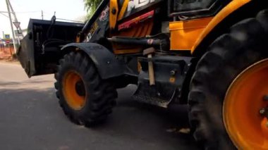 Köy caddesi boyunca siyah ve turuncu kazıcı sürüyor.