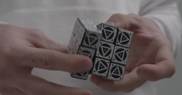 Man solves Rubik cube with triangles on light background — Stock Video