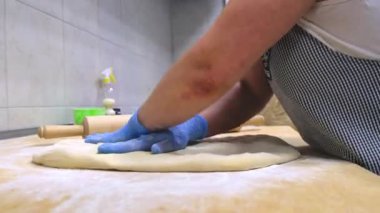 Eldivenli fırıncı ve önlüklü hamur yoğurur ahşap masada.