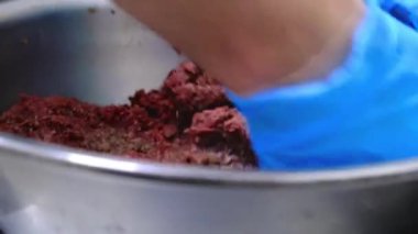 Çalışan büyük metal kasede kıymalı et karıştırıyor.