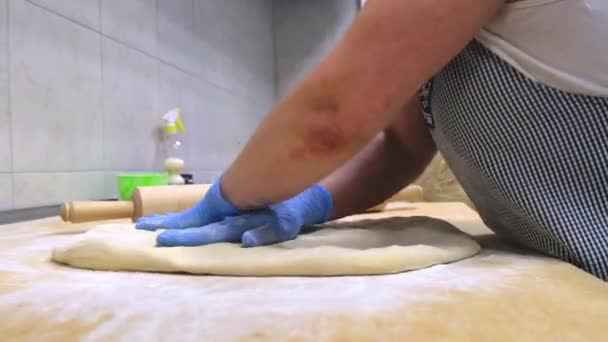 Baker in handschoenen en schort kneedt deeg op houten tafel — Stockvideo