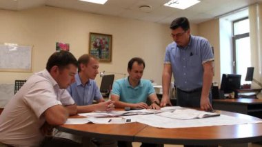 Mühendislerden oluşan bir ekip şirket ofisinde çizimlerle çalışıyor.