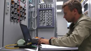 Teknisyen alt istasyonda dizüstü bilgisayar kontrol ekipmanları üzerinde çalışıyor.