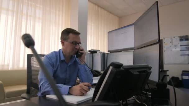 Trabalhador fala por telefone sentado perto do computador na sala de controle — Vídeo de Stock