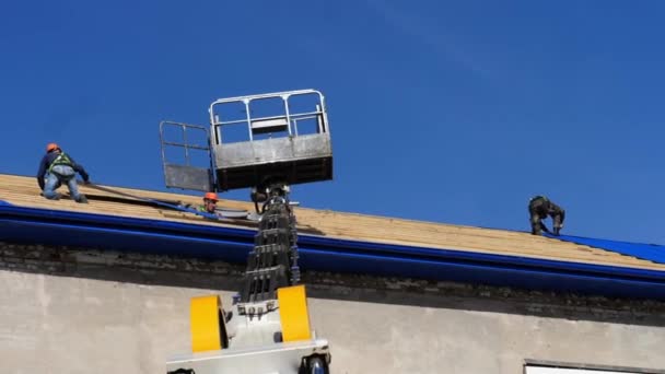 Les travailleurs posent des feuilles bleues sur le toit et le berceau de levage à proximité — Video