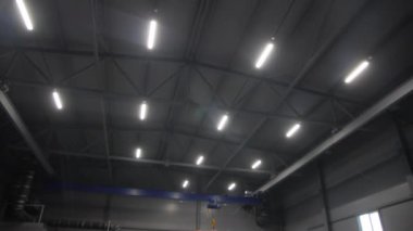 Geniş bir depoda yüksek tavanda parlayan lambalar.