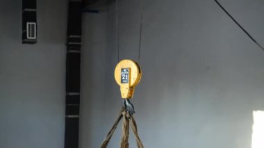 Geniş atölyede ağır kargo sarı kancaya asılı.