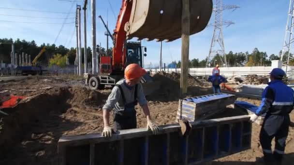 Ludzie kontrolują szczegóły betonu przenoszone przez koparkę na miejscu — Wideo stockowe