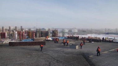Turuncu yelekli inşaatçılar stadyum inşaatında çalışıyorlar.