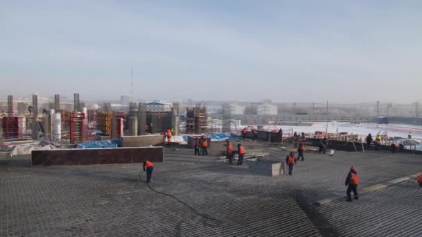 Строители в оранжевых жилетах работают на стройплощадке стадиона — стоковое видео